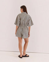 Back view of a woman wearing a House of Holabox Ingrid striped cotton-blend playsuit with a tie waist and collar.