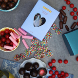 House of Holabox Sweeta chocolate freckles in a heart-window gift box surrounded by assorted colorful candies.