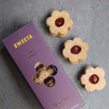 House of Holabox SWEETA Jam Kisses, flower-shaped vegan raspberry jam biscuits with icing sugar, next to purple box.