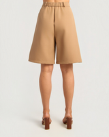 House of Holabox tan Bermuda long line shorts featuring an elasticated back waistband, worn with brown block heels.