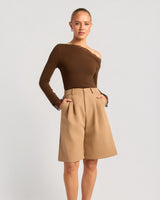 House of Holabox tan high-waisted Bermuda shorts with front pleats, belt loops, and pockets on a model