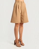 House of Holabox tan high-waisted Bermuda shorts with front pleats and tailored longline fit on a model
