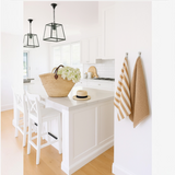 House of Holabox Mama and Tochter French linen tea towel with wide toffee stripes hanging in a bright white kitchen