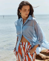 House of Holabox Val oversized pale blue lyocell-blend shirt worn open over striped trousers at the beach