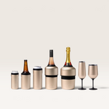 Huski Slim Can Cooler in metallic gold stainless steel with black silicone grip and base, shown with various drink bottles and glasses.