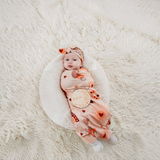 Baby wrapped in an ArchNOllie Love Bug jersey swaddle with matching headband and wooden milestone disc on a rug.