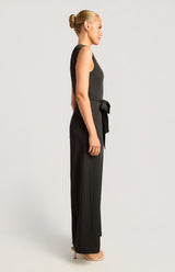 Jasmine Front Pleat Jumpsuit in black, featuring a sleeveless silhouette and a polished gold buckle waist detail.