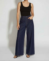 Woman wearing a black tank top and blue wide-leg pants against a white background