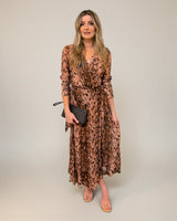 Model wearing an Isla wrap dress in a brown abstract print with a collared neckline, self-tie waist, and fluid midi skirt.