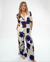 Woman wearing wide-leg cream satin pants with a blue and dark floral print and matching button-up shirt.
