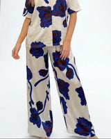 Wide-leg satin pants in cream with a bold blue and dark floral print, featuring a comfortable elastic waistband.