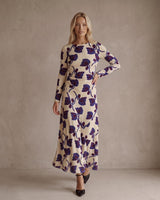 Model wearing a cream long-sleeve jersey dress with a dark blue floral print, boat neckline, and gathered waist detail.
