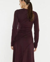 Back view of a dark burgundy jersey dress featuring a boat neckline, long sleeves, and gathered waist detail.