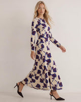 Model wearing a cream long-sleeve jersey dress with a blue floral print, boat neckline, and gathered waist detail.