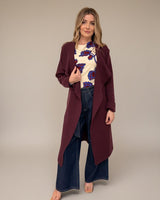 Woman wearing a cream jersey top with a blue and red floral print, layered under a long, burgundy open-front coat.