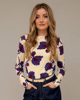 Woman wearing a floral sweater and dark pants against a neutral background