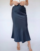 Navy blue bias-cut midi slip skirt with an elasticated waistband, styled with a white top and clear heels.
