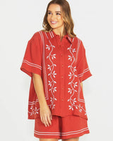 Woman wearing rust-colored 100% cotton shorts with an elastic drawstring waist and white vine embroidery.