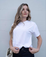Woman wearing a crisp white cotton-blend crew neck tee with a subtle front knot detail, styled with dark denim jeans.