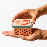 Two hands holding a small wooden stamp with a red design on a white background