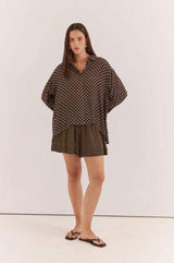 Model wearing a relaxed-fit, long-sleeve Joy Shirt in brown viscose with a white polka dot print and button-up collar.