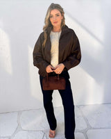 Woman wearing a brown leather-look bomber jacket with a high neck, zip front, and relaxed fit over a cream sweater.