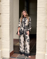 Woman wearing a June collared shirt in a black and cream floral print with contrast trim and matching wide-leg trousers.