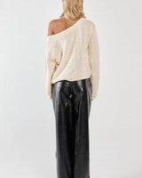 Cream-colored 100% cotton textured knit sweater with an asymmetric neckline, worn with black trousers.