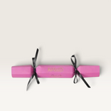 Kip&Co pink gift cracker with black ribbon ties, featuring gold branding on a smooth cylindrical paper exterior.
