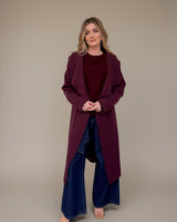 Relaxed-fit wine colored coatigan with a draped open front and practical pockets, worn over a matching sweater.