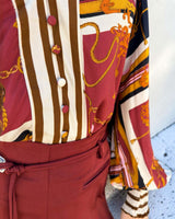 Lauren blouse in 100% rayon featuring a burgundy, cream, and gold chain print with a button-up front and striped cuffs.