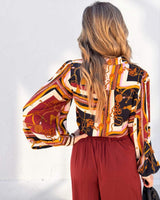 Woman wearing a long-sleeve Lauren blouse in a multi-colored chain print rayon fabric with deep red trousers.