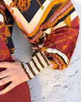 Lauren blouse in 100% rayon featuring a burgundy, gold, and black chain print with long sleeves and striped cuffs.