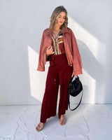 Woman wearing a long-length Lauren blouse with a colorful print, paired with a dusty pink jacket and burgundy trousers.