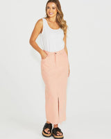 Woman wearing a peach-colored cotton maxi pencil skirt with a front button, zip, and pockets, paired with a white tank top.