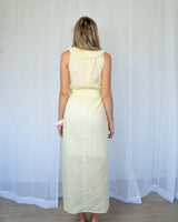Back view of a pale yellow cotton sundress featuring a ruffled neckline and a self-tie waist belt.