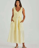 Model wearing a pale yellow cotton midi sun dress with a ruffled neckline, self-tie waist belt, and side pockets.