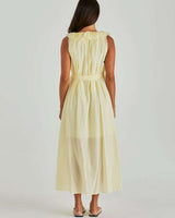 Back view of a pale yellow cotton midi sun dress with a ruffled neckline and a self-tie waist belt.