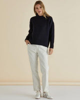 Navy blue mock neck knit jumper with ribbed cuffs and hem, styled with white trousers and sneakers.