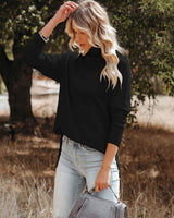 Woman wearing a black high-neck knit sweater with ribbed cuffs and a stepped hem, styled with light wash jeans.