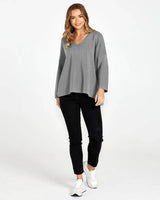 Woman wearing black Luella stretch jeans with mock pockets, paired with a grey V-neck sweater and white sneakers.
