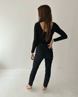 Woman wearing black Luella stretch jeans with mock back pockets and a fitted black long-sleeve top against a white wall.