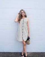 Minimalist cream shift dress with black vertical stripes, featuring a functional button-front and side pockets.