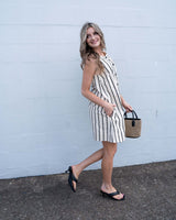 Woman wearing a beige and black striped cotton-blend shift dress with a button-front, side pockets, and a relaxed fit.