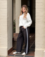 Woman wearing black Maddison joggers with a white side stripe, elasticated waistband, and relaxed fit.
