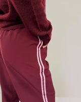 Wine-colored Maddison joggers featuring a relaxed fit, side pockets, and a contrasting light pink side stripe.