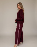 Woman wearing wine-colored relaxed fit joggers with side stripe detail and a matching long-sleeve sweater.