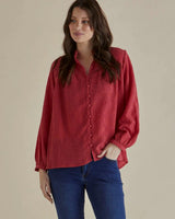 Red crinkle fabric Marie blouse with a button-up front, long sleeves, and buttoned cuffs paired with blue jeans.