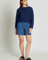 Woman wearing a navy blue textured acrylic knit sweater with long sleeves and a crew neck paired with denim shorts.