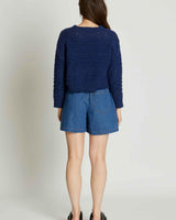 Back view of a navy blue textured acrylic knit sweater with long sleeves paired with denim shorts.